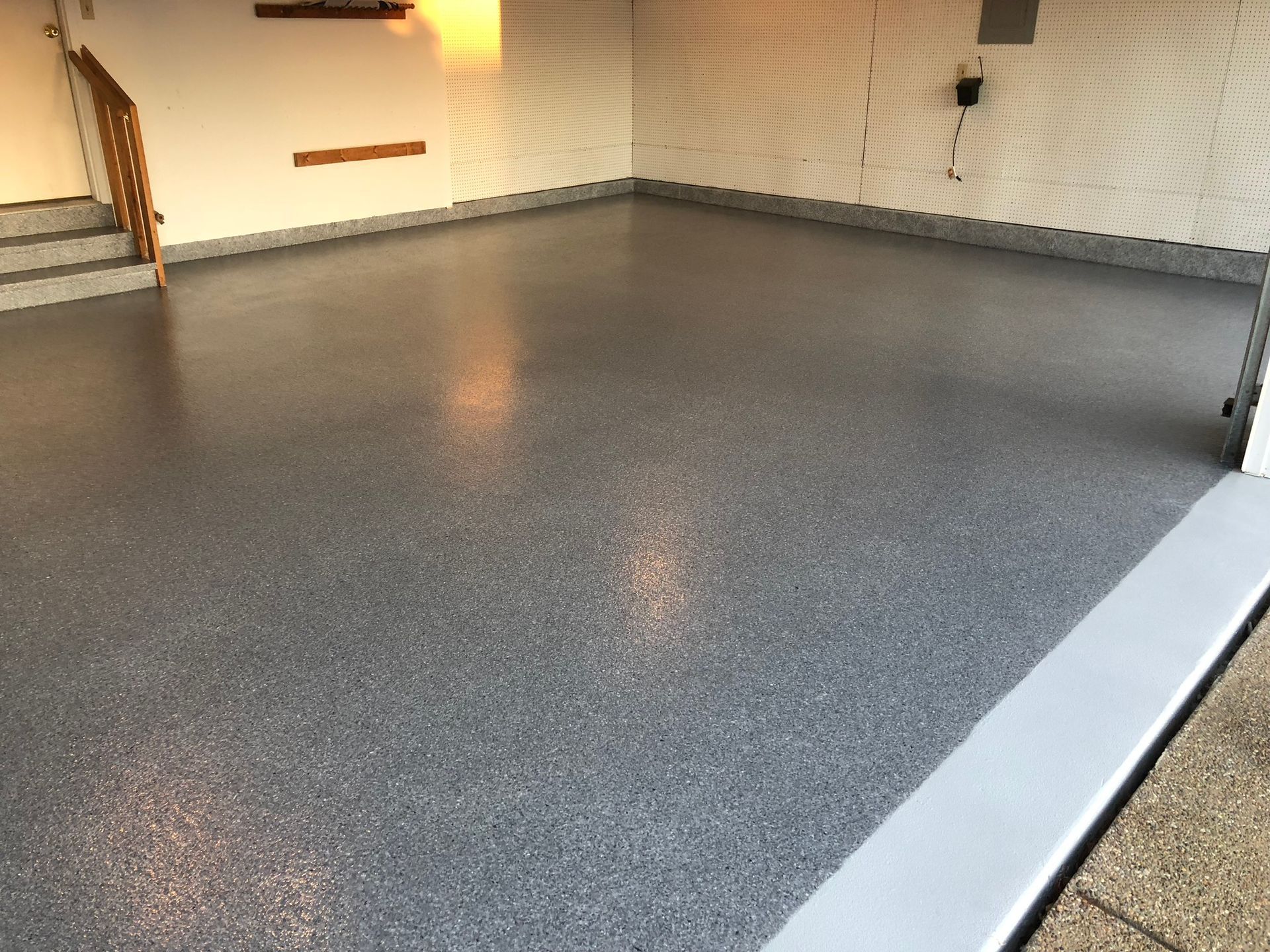 Empty garage with gray epoxy floor and white walls, lit by warm lights.