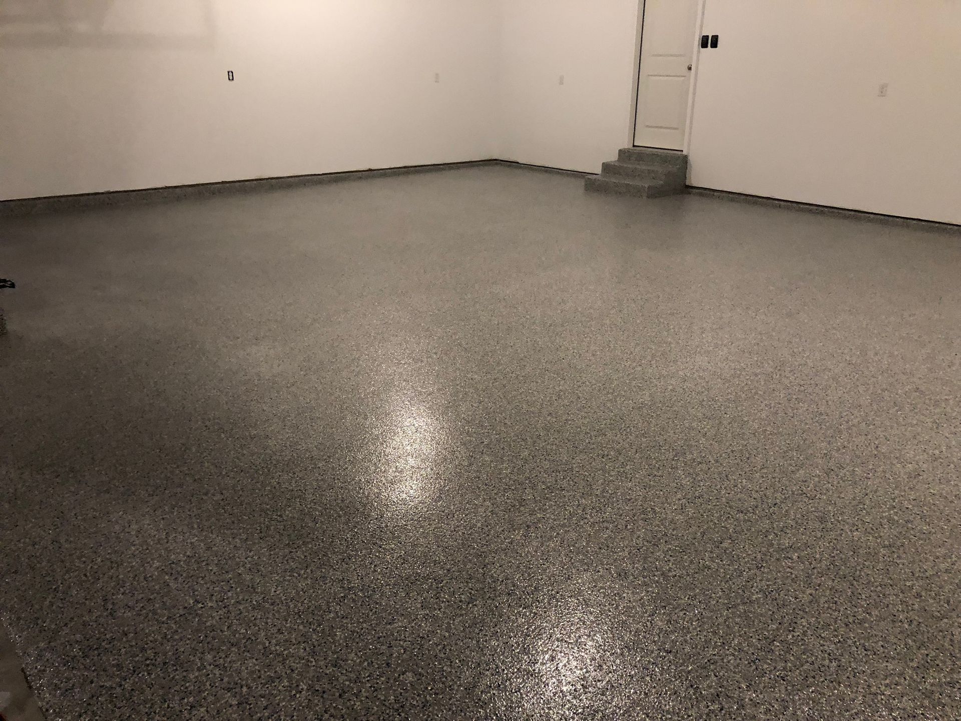 Empty gray epoxy-floored room with white walls and a small stairway in the corner
