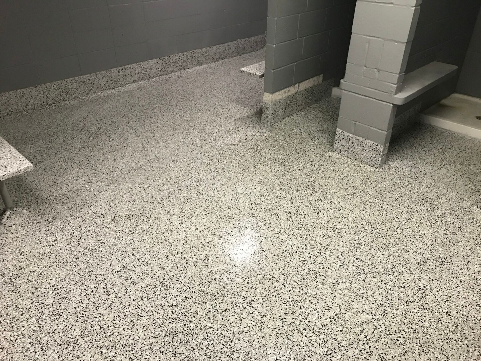 Speckled gray restroom floor with stalls and partitions visible in the background