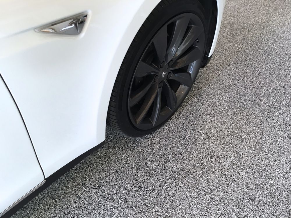 Close-up of a white car’s front wheel and fender on gray pavement