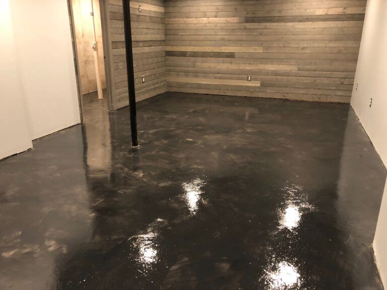 Empty basement with wet black concrete floor and exposed wooden support posts.