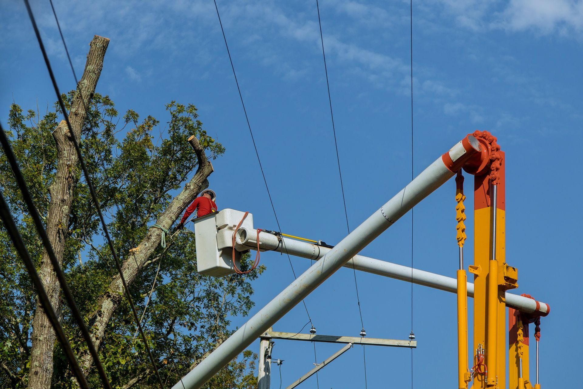 Utility worker in bucket lift repairing overhead power lines against a blue sky