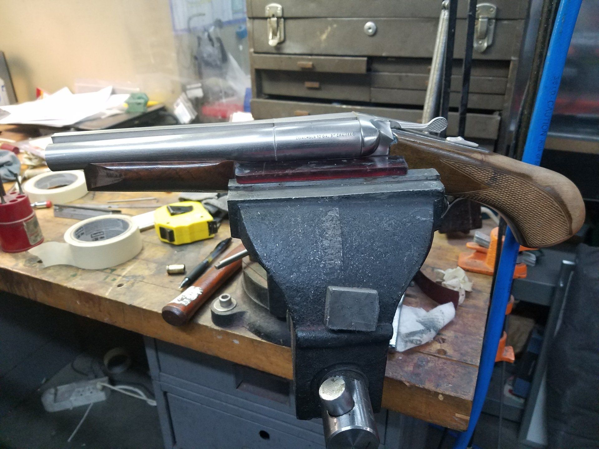 A handgun clamped in a vise on a workbench, with wood and tools.