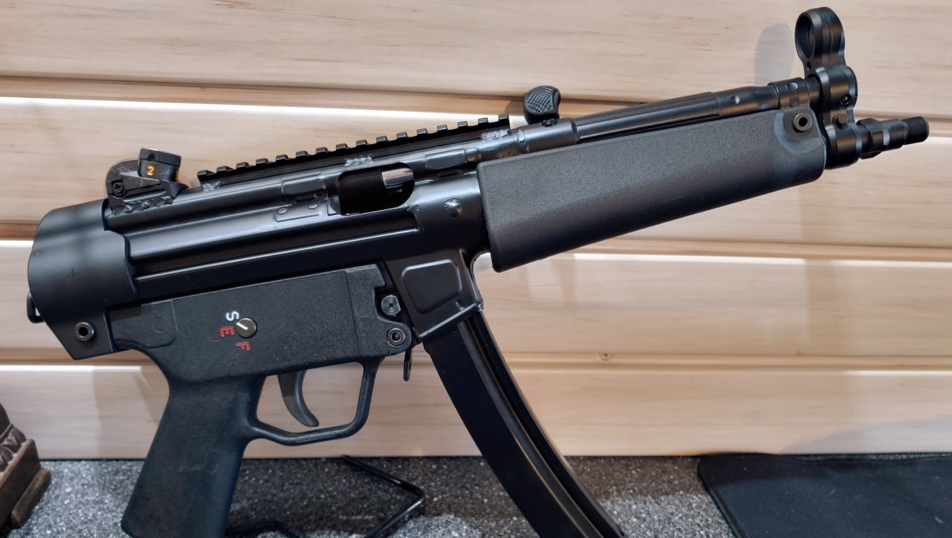 Black submachine gun with a magazine, rail, and sights, on a wooden surface.