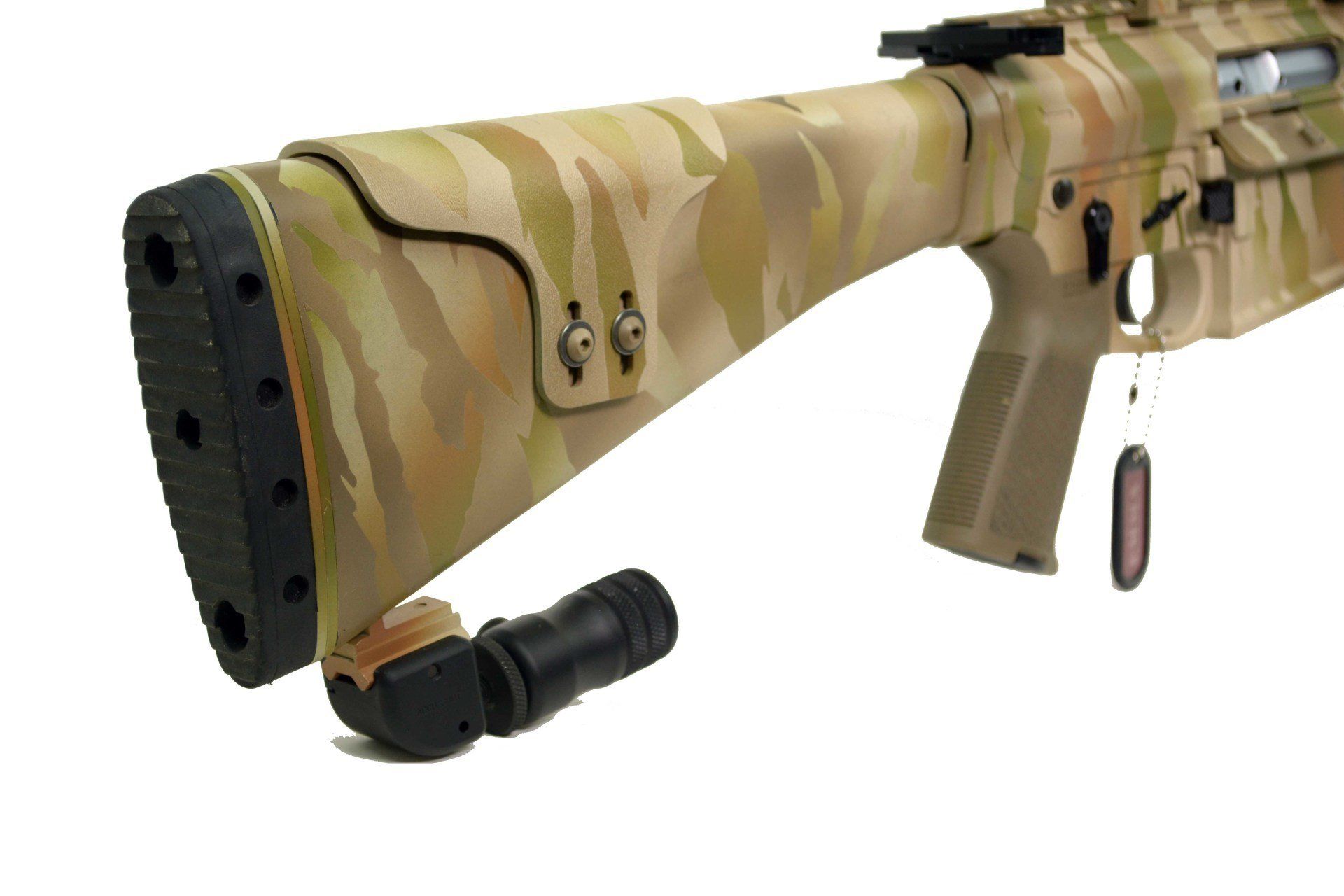Close-up of a tan and brown camouflage rifle buttstock and an attached, detached black component.