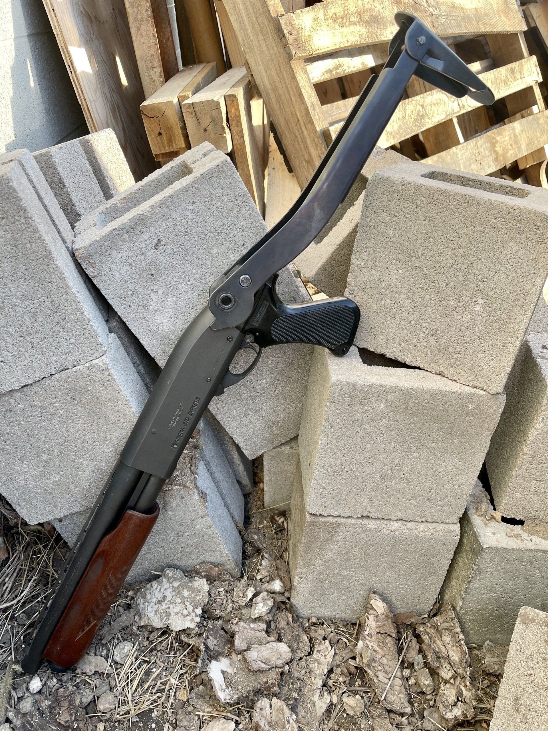 Shotgun with a folding stock and wooden forend, resting on cinder blocks.