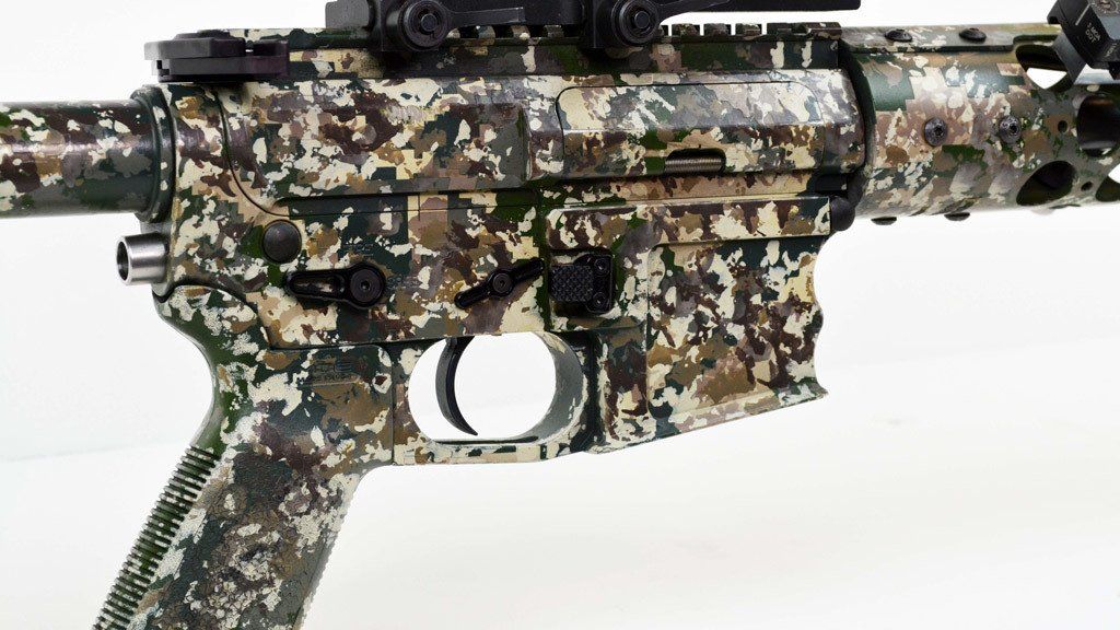 Camouflaged rifle with black trigger and sights.