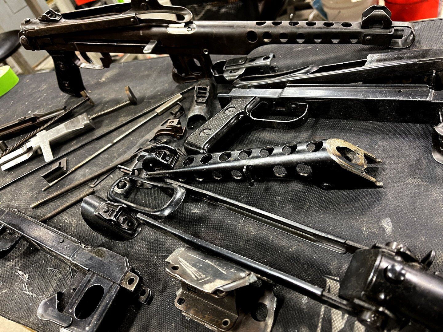 Disassembled firearm parts on a dark surface, including a barrel, stock, and various internal components.