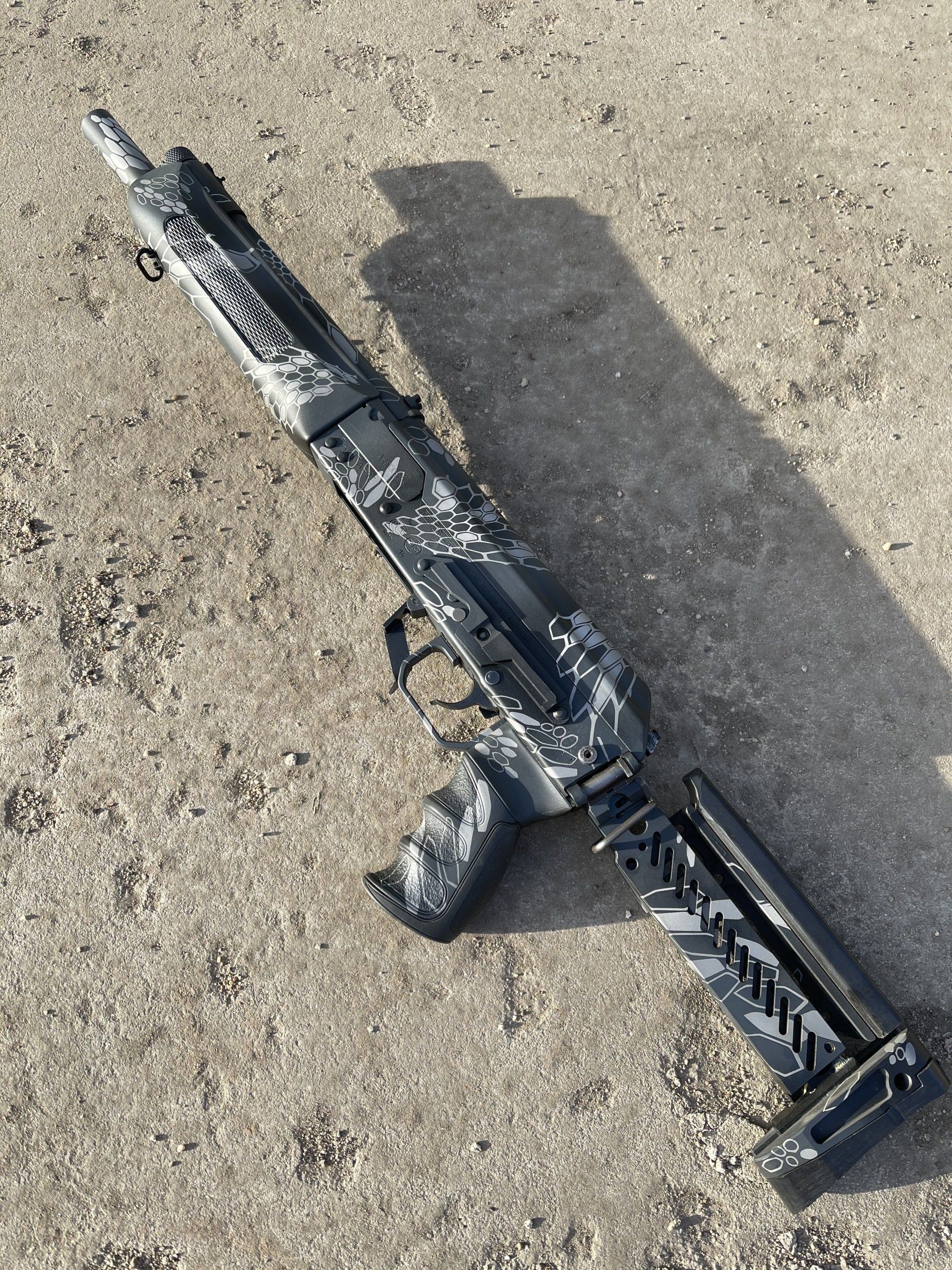 Black and white camouflage shotgun on a concrete surface.