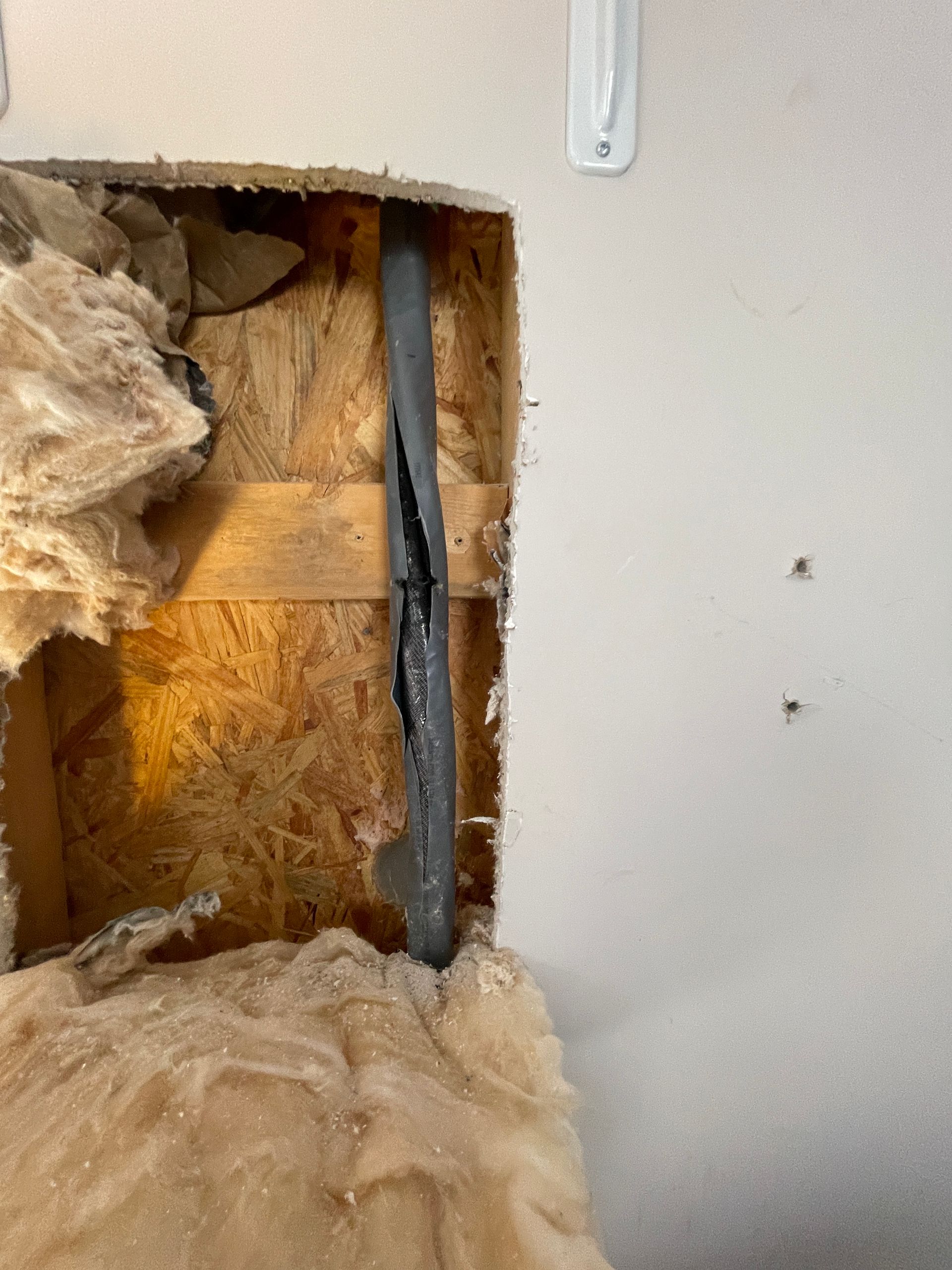 Hole in wall reveals a damaged pipe, insulation, and wood framing.