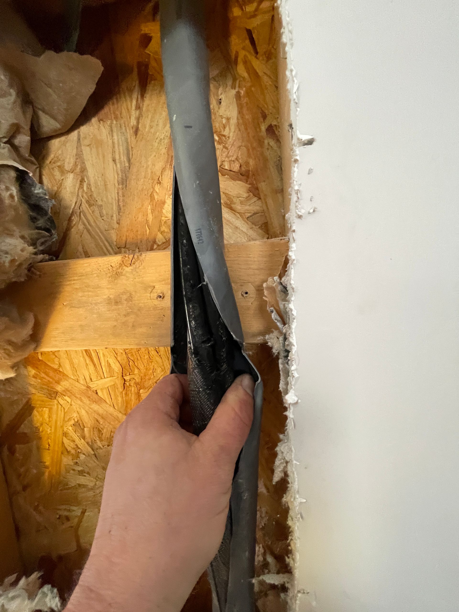 Hand holding damaged flexible ductwork in a wall cavity, wood framing visible.