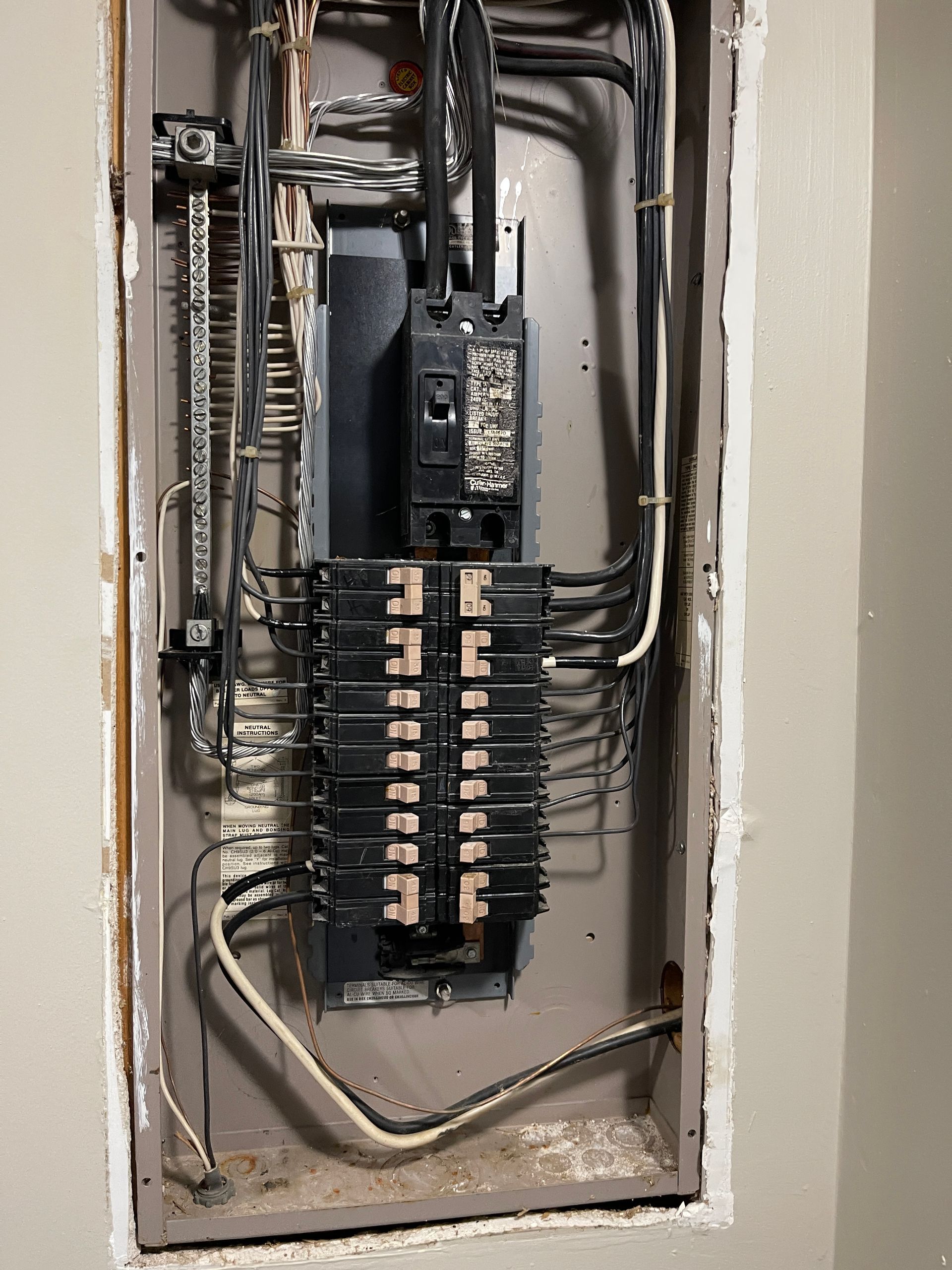 Electrical panel with numerous circuit breakers and wiring inside a recessed wall.