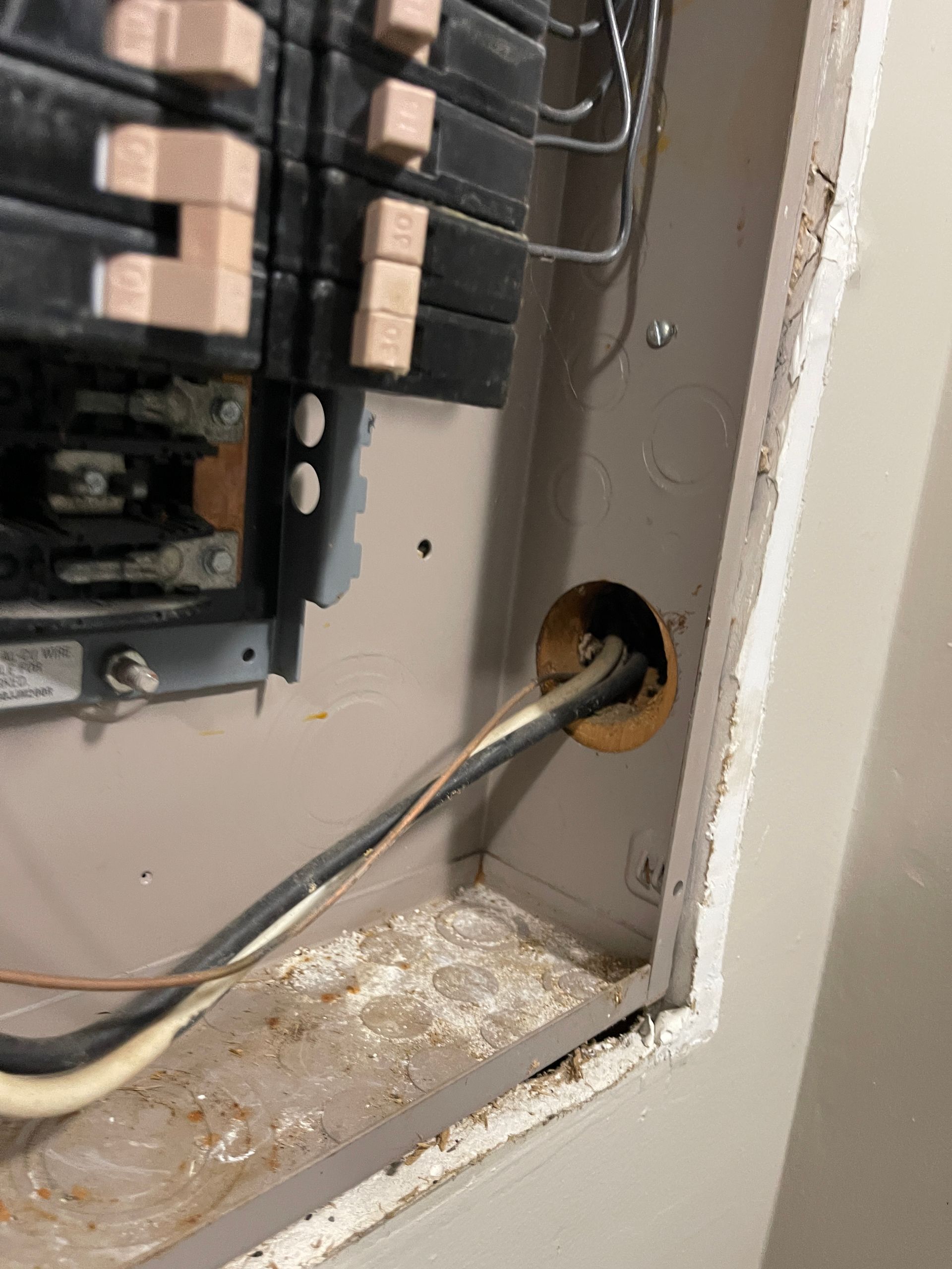 Open electrical panel with wires entering. Gray and beige tones, dust visible.