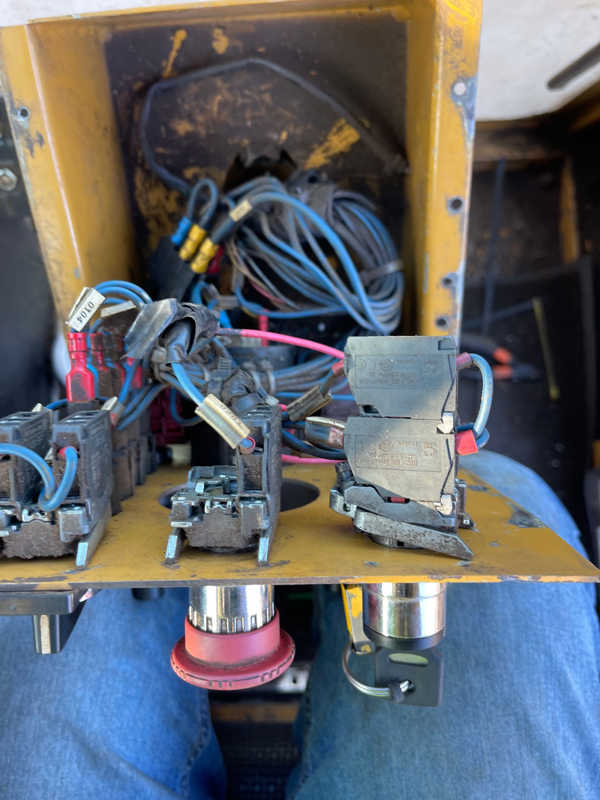 Damaged electrical panel with burnt components, wires, and two red push buttons, in a yellow box.