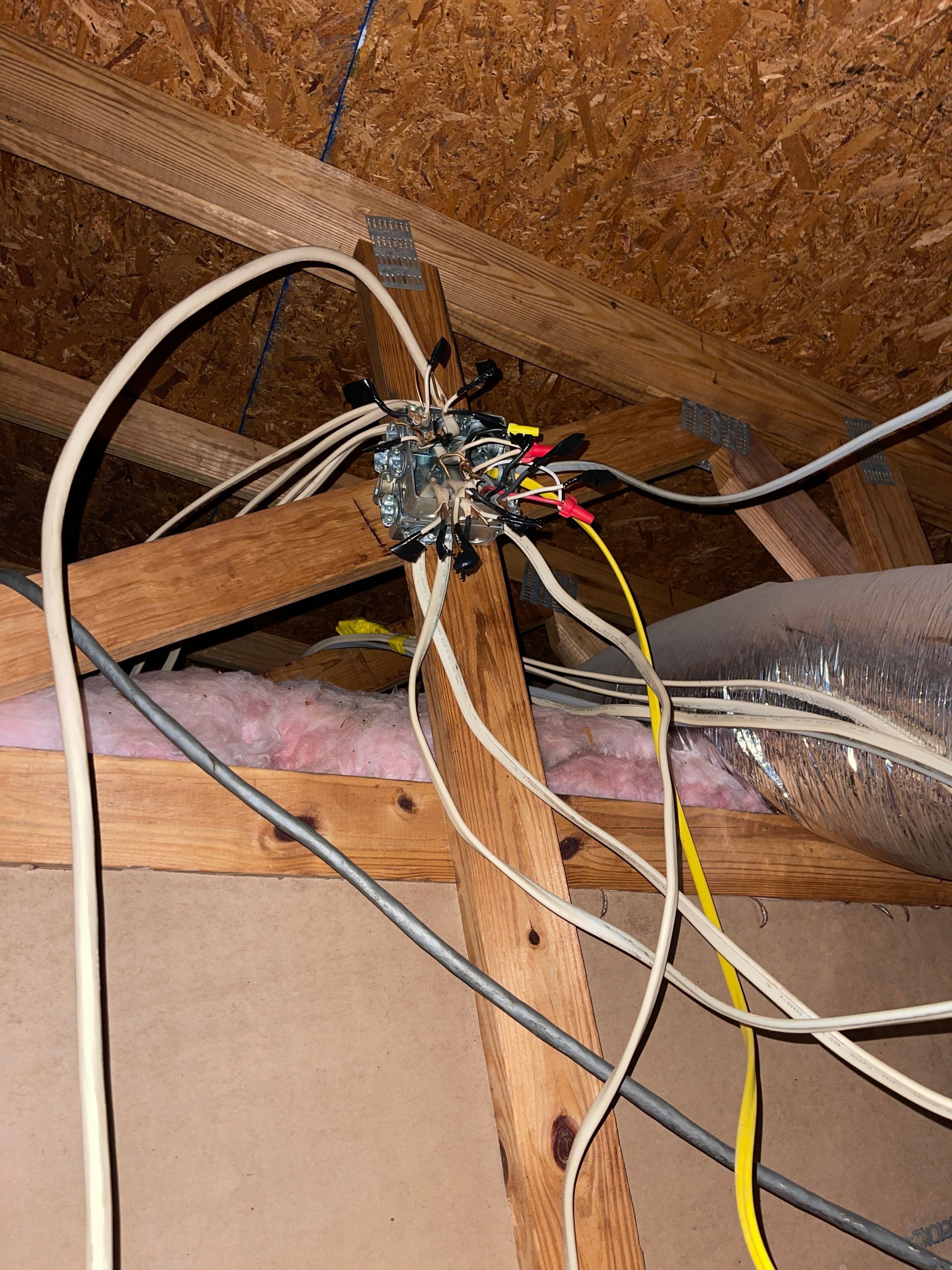 Electrical junction box in an attic with various wires and wooden beams.