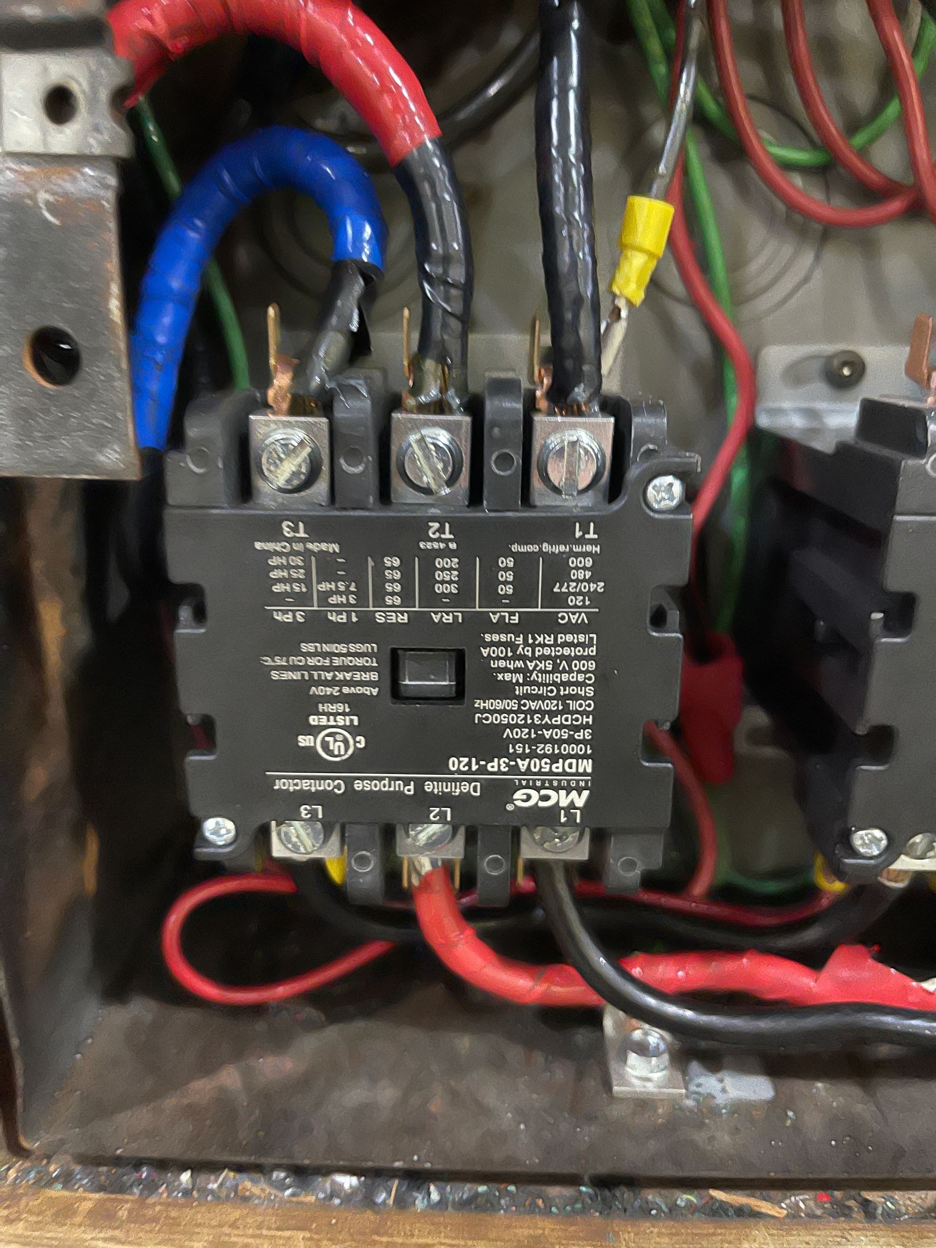 Black electrical contactor with red, blue, and black wires attached inside a metal enclosure.