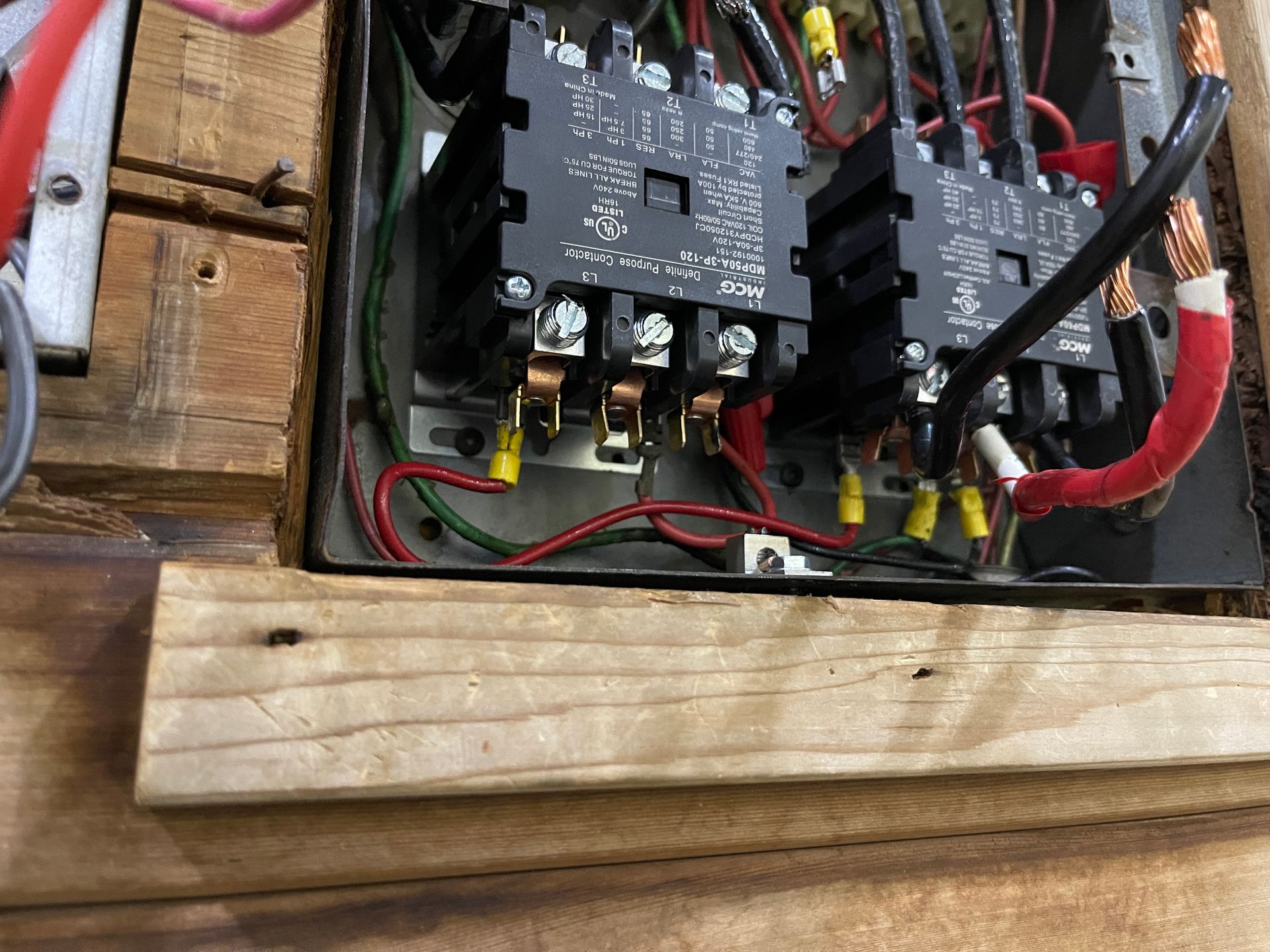 Electrical panel with two black relays, wires, and wooden frame.