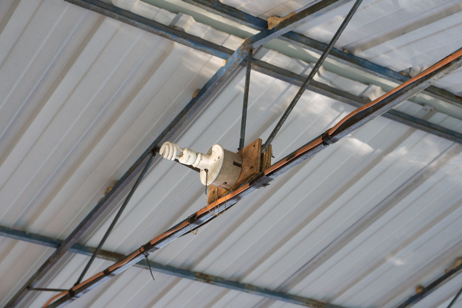 White light fixture attached to a metal beam ceiling.