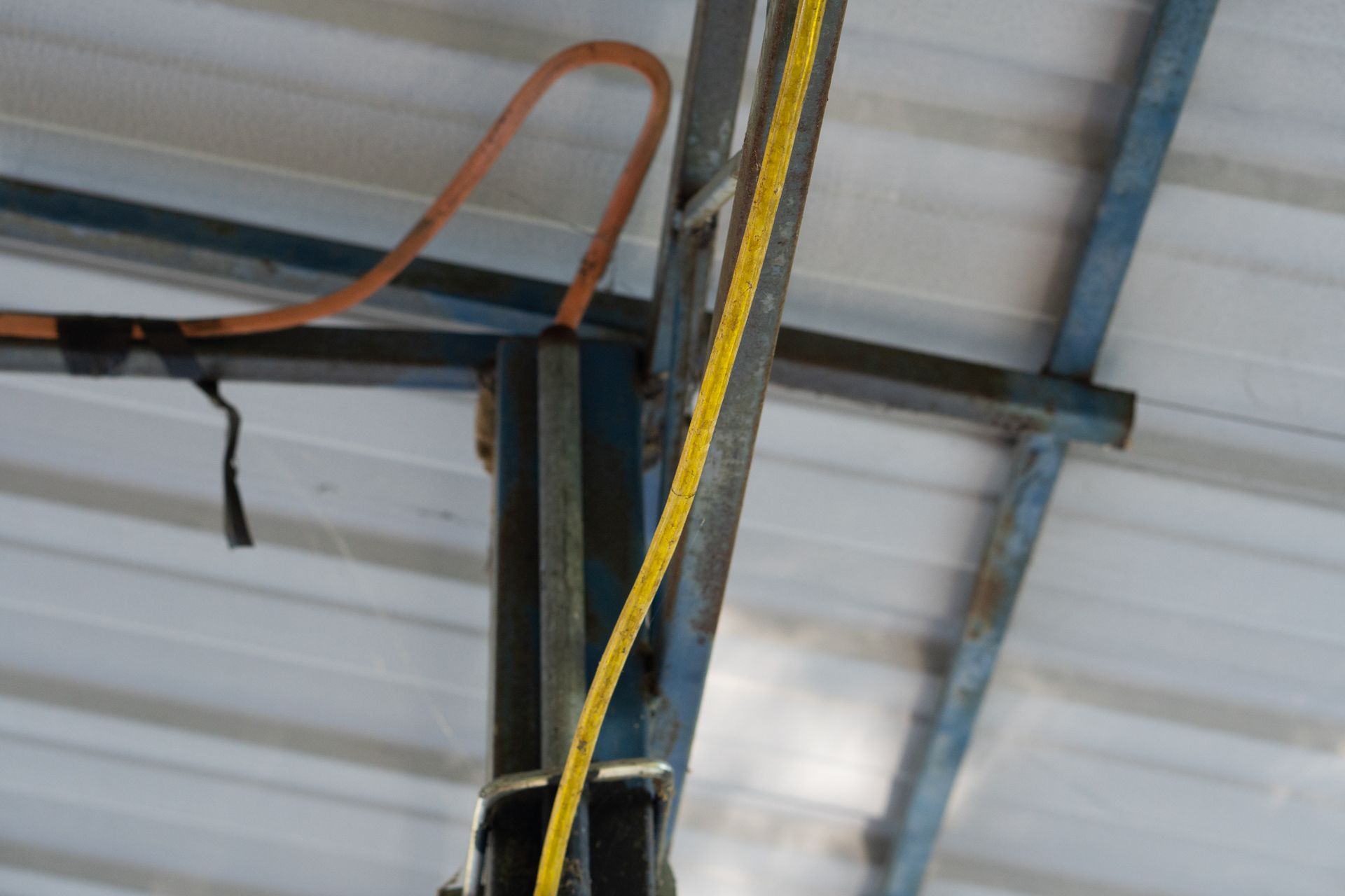 Yellow electrical wire and brown hose run along blue metal beams of a roof.