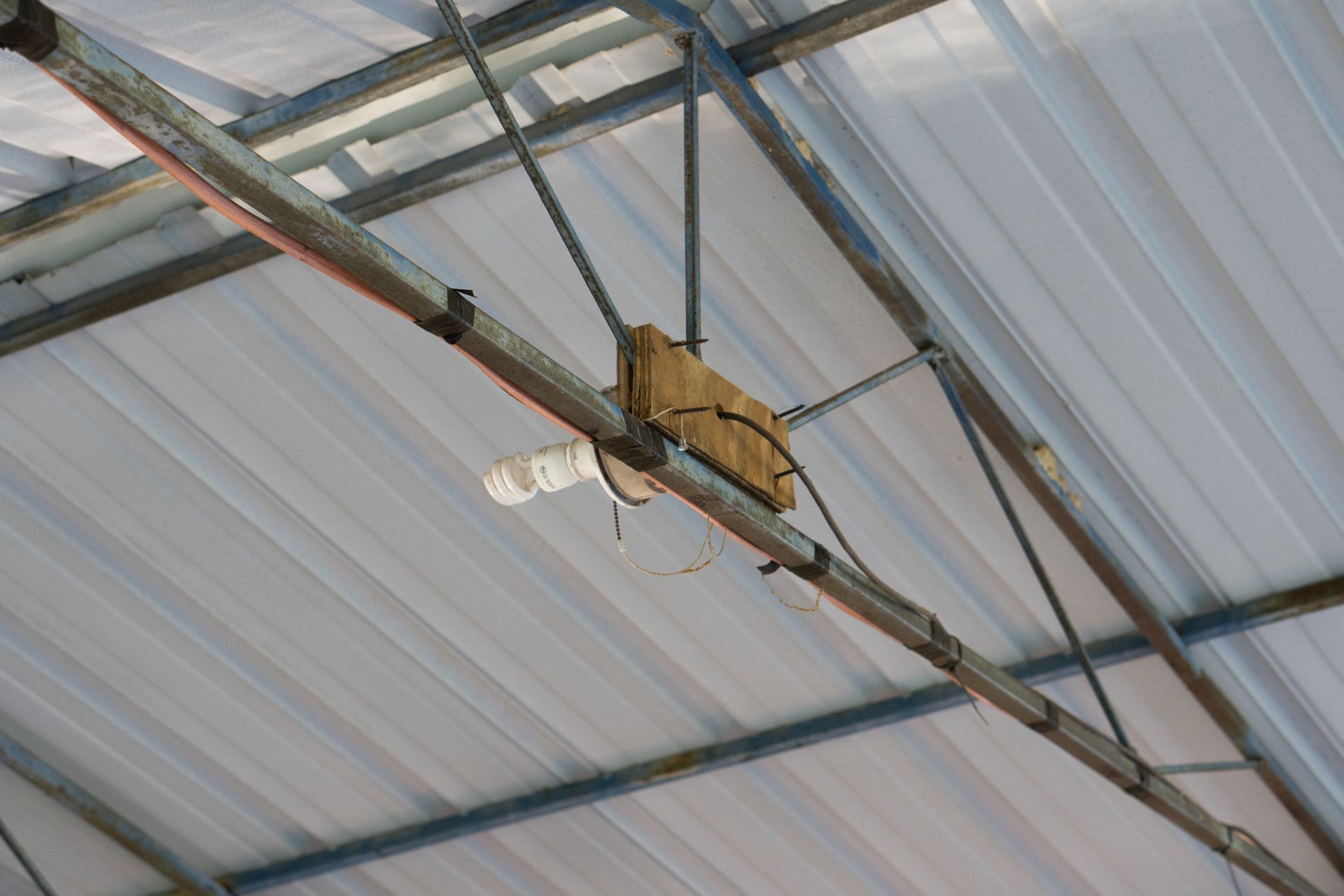 Motorized mechanism attached to metal beams inside a corrugated roof structure.