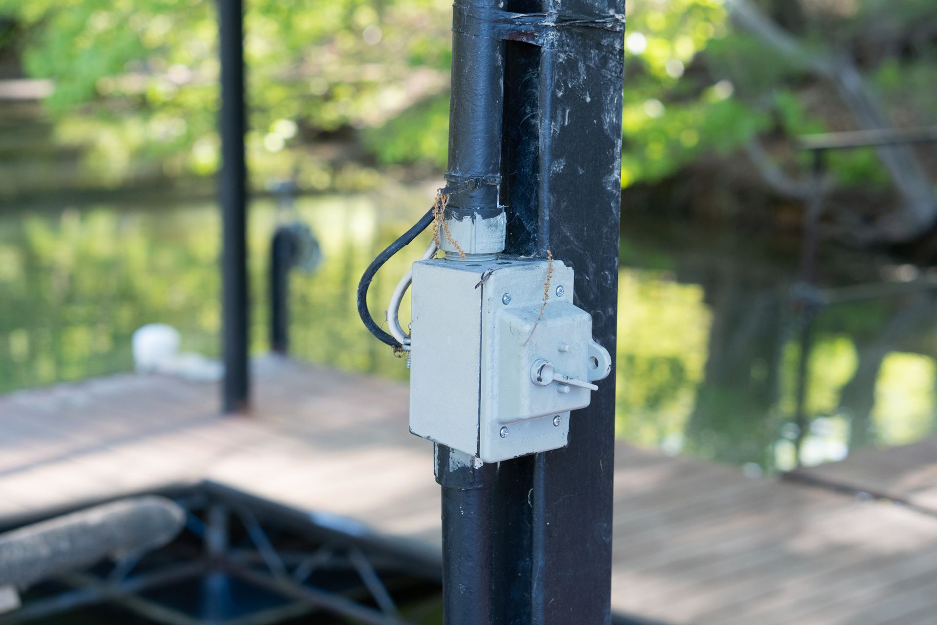 Gray electrical box on a black pole; a water dock is in the blurred background.