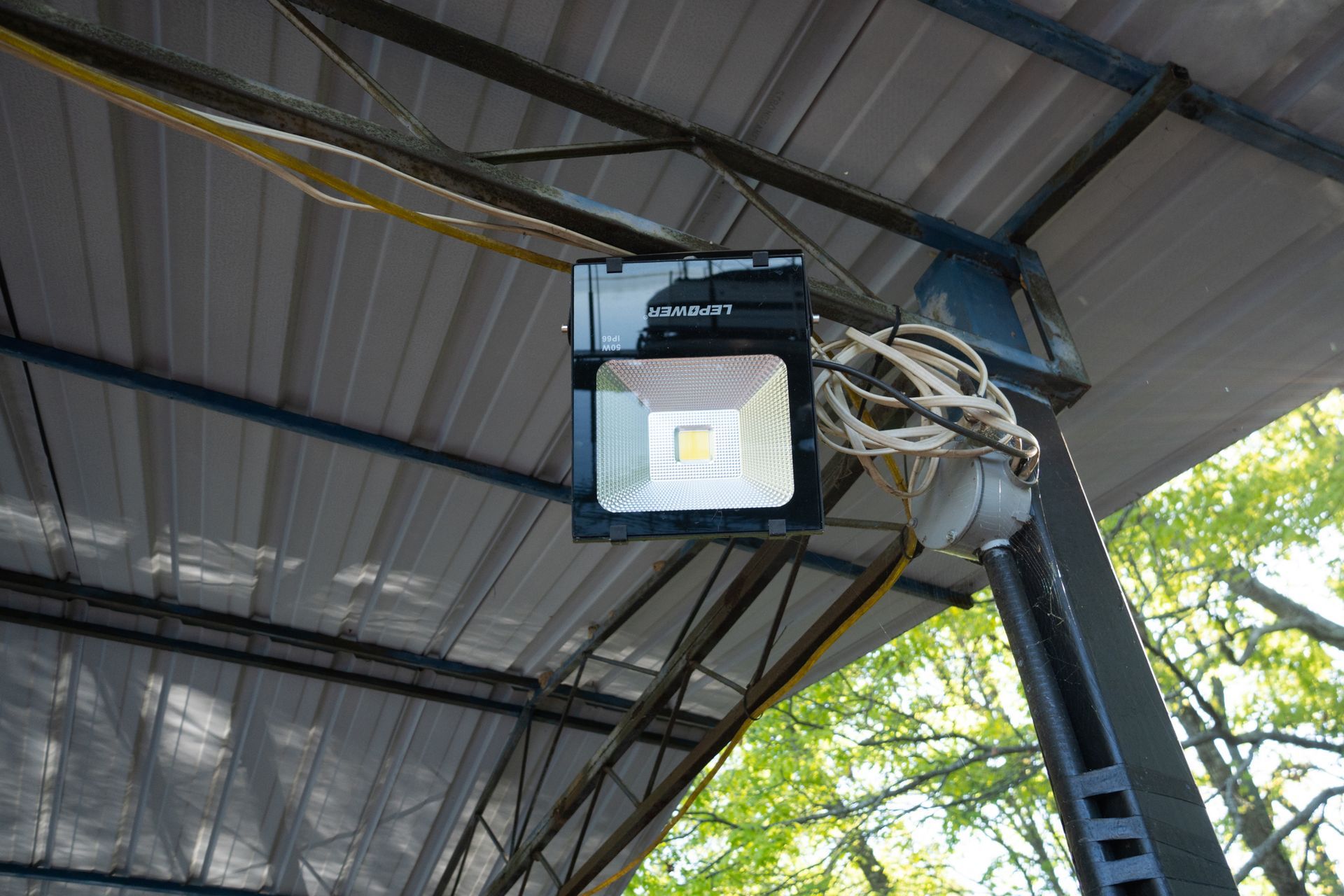 LED floodlight mounted under a metal roof, with tangled wires visible.