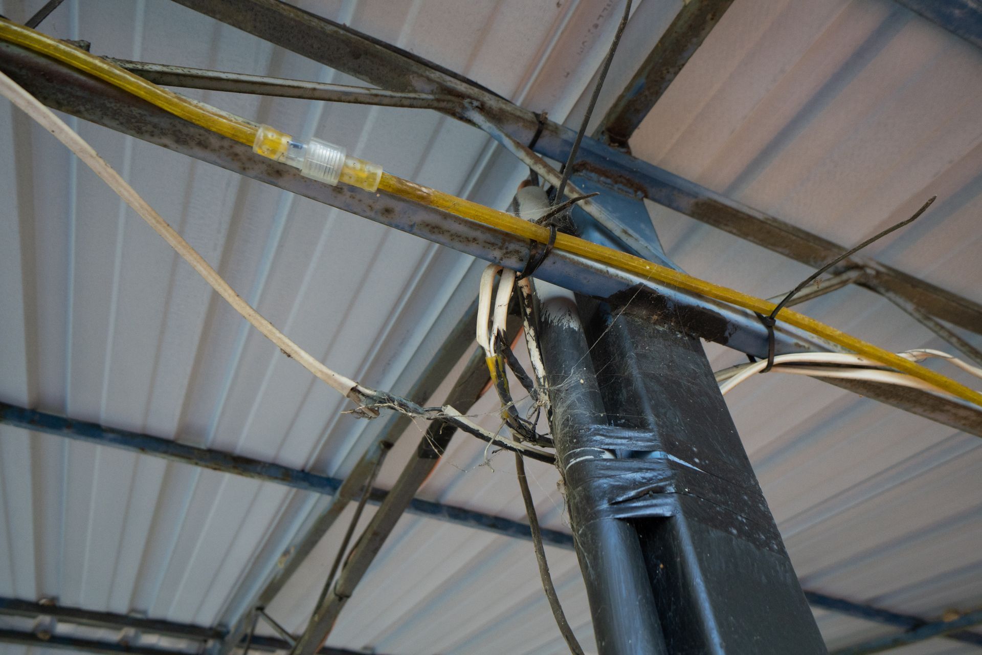 Steel support beam with overhead wiring, zip-tied to a steel structure under a metal roof.