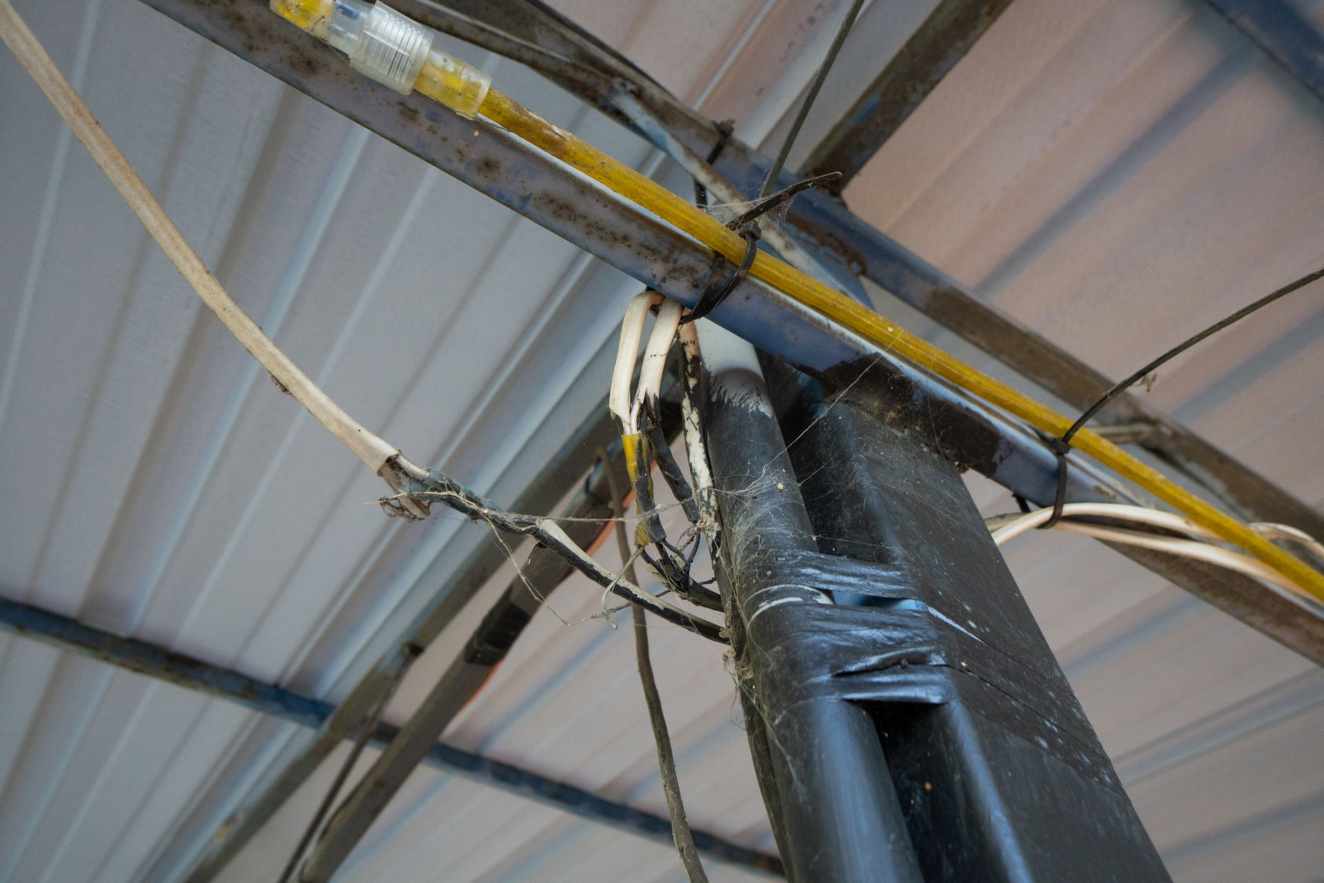 Overhead view of metal beams and electrical wires running along the roof of a building.