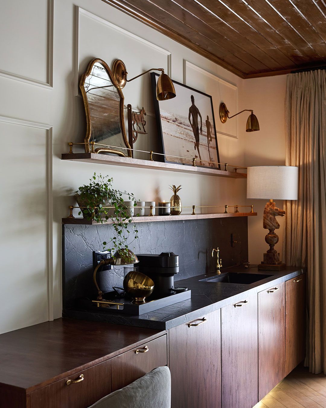 Stylish sideboard with mirror art, brass lamps, plants, and a table lamp in a warm, elegant room