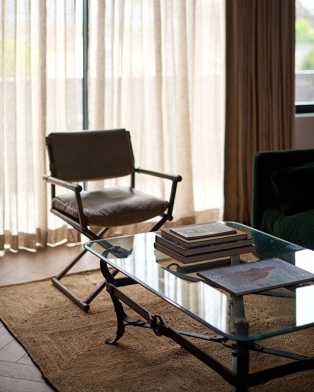 Brown chair beside glass coffee table with stacked books in a sunlit living room