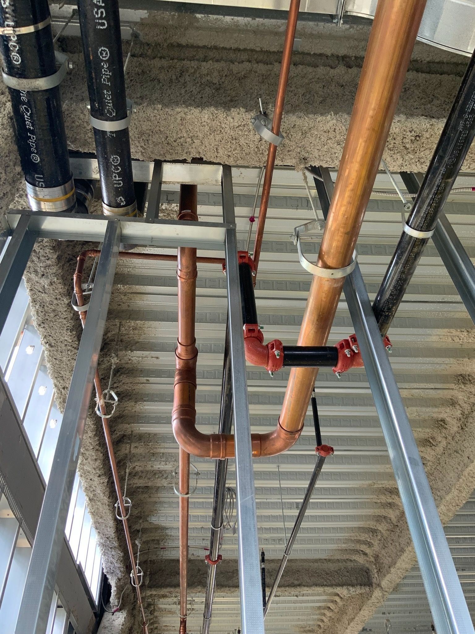 Ceiling view of exposed copper and black pipes running through a metal-framed industrial interior.