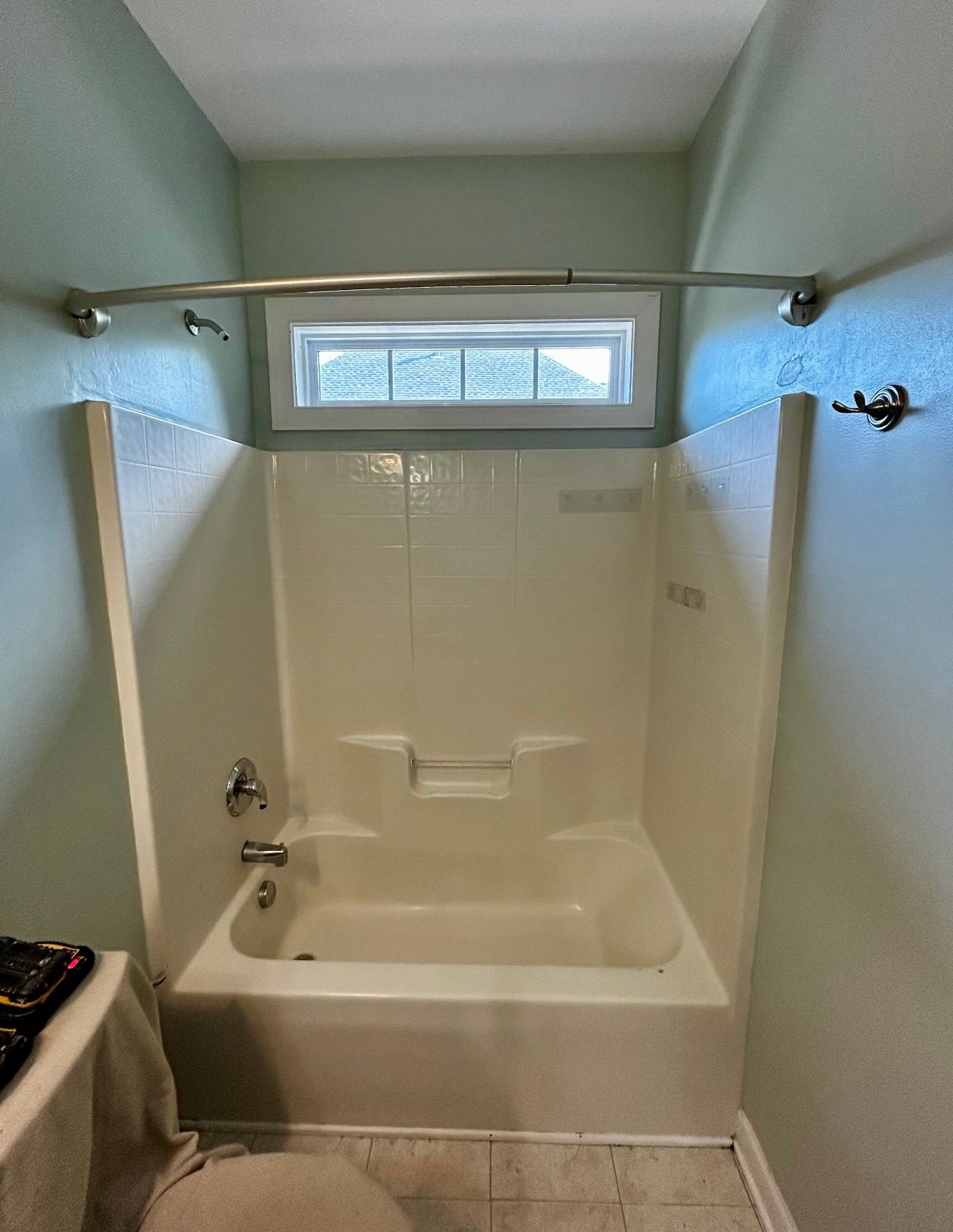 Bathroom with white tub-shower, tiled surround, frosted window, and shower curtain rod above.