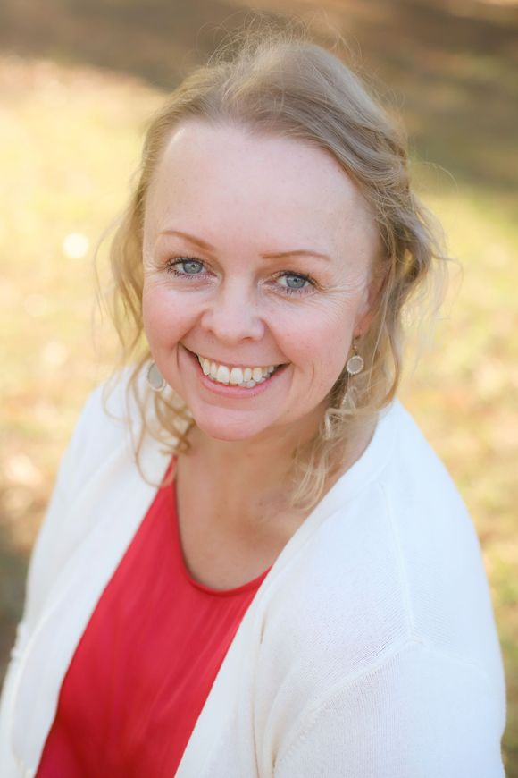 A woman in a blue shirt is smiling in front of a body of water.