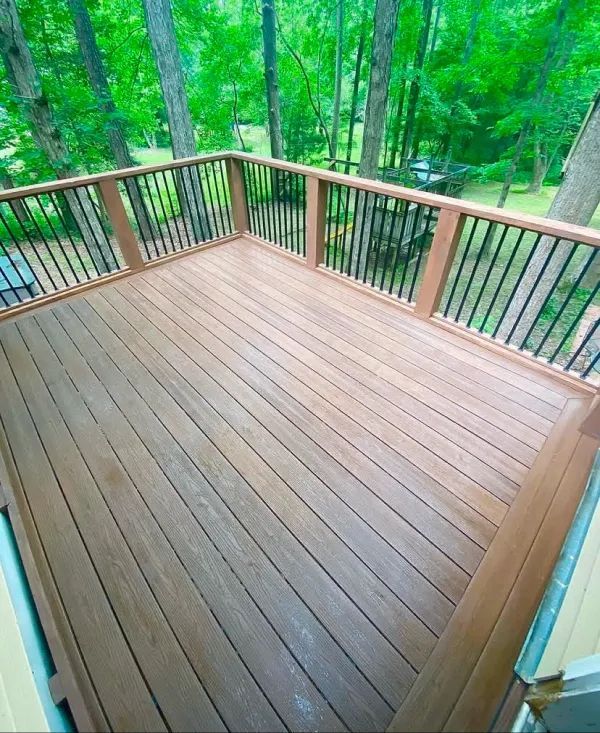 A wooden deck with a metal railing and trees in the background