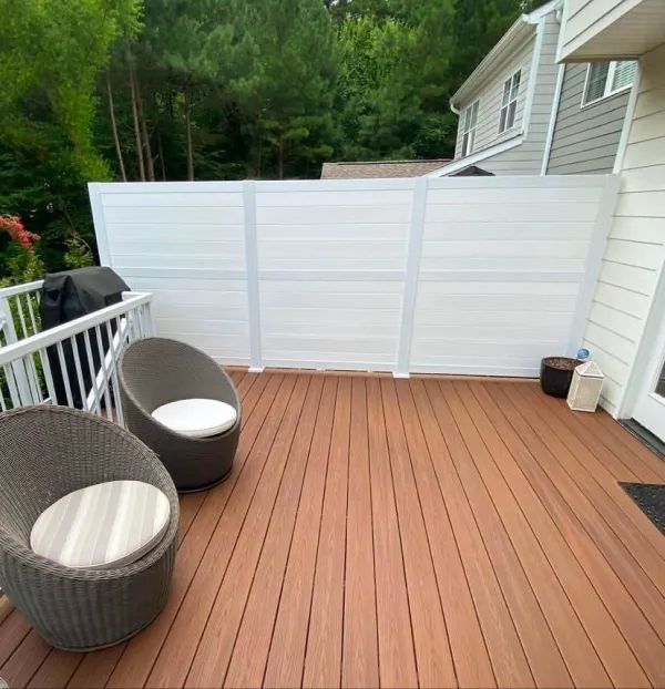 A wooden deck with two chairs and a white fence