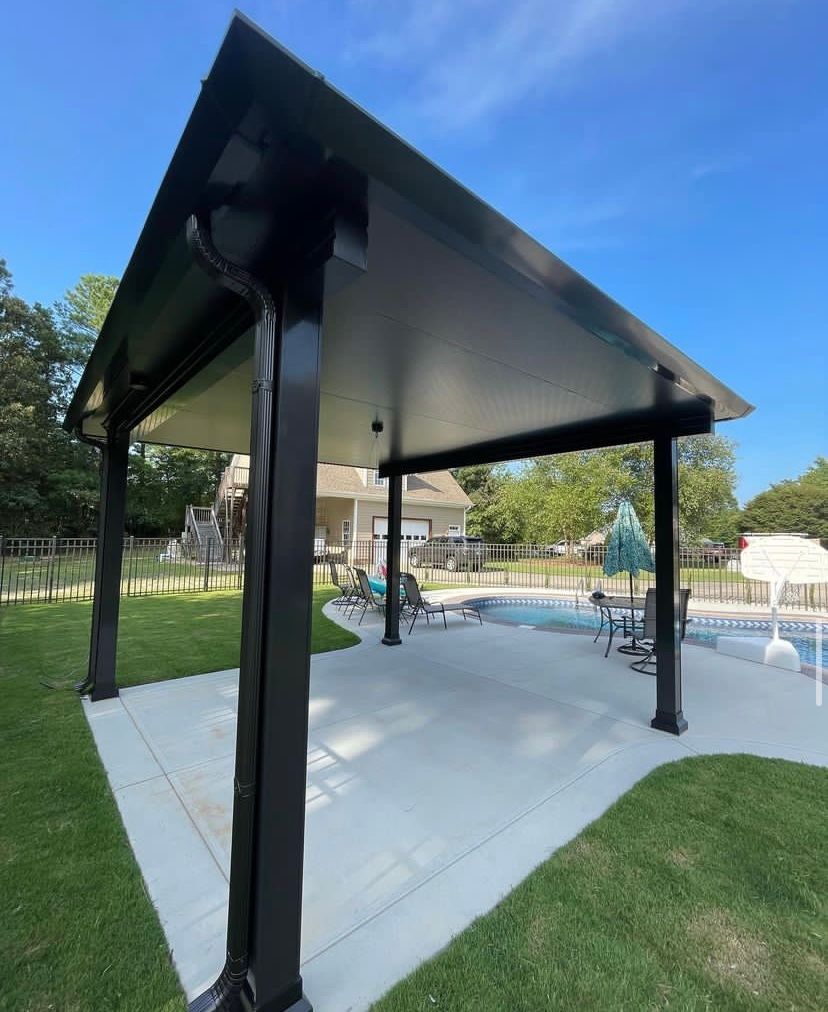 A black covered patio area with a pool in the background