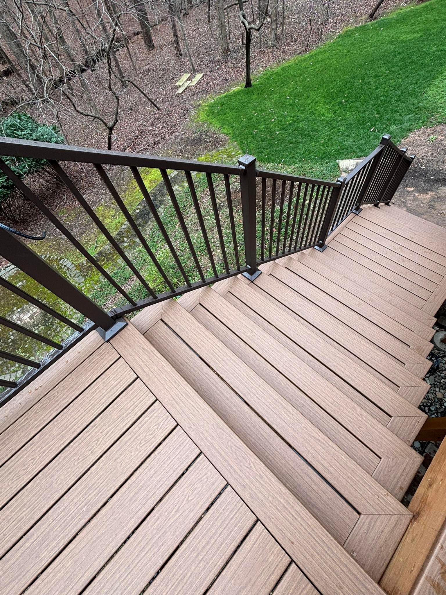 Wooden outdoor staircase with dark brown railing leads down to a grassy area