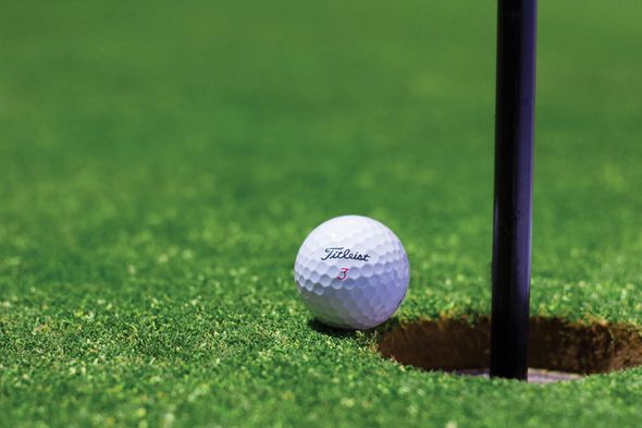 Golf ball near the edge of the hole on a green golf course, with the black flag pole visible. La Huerta Golf Tournament