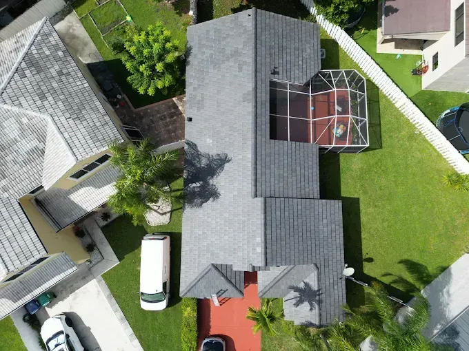 Two roofers installing dark gray tiles on a roof, blue sky backdrop.