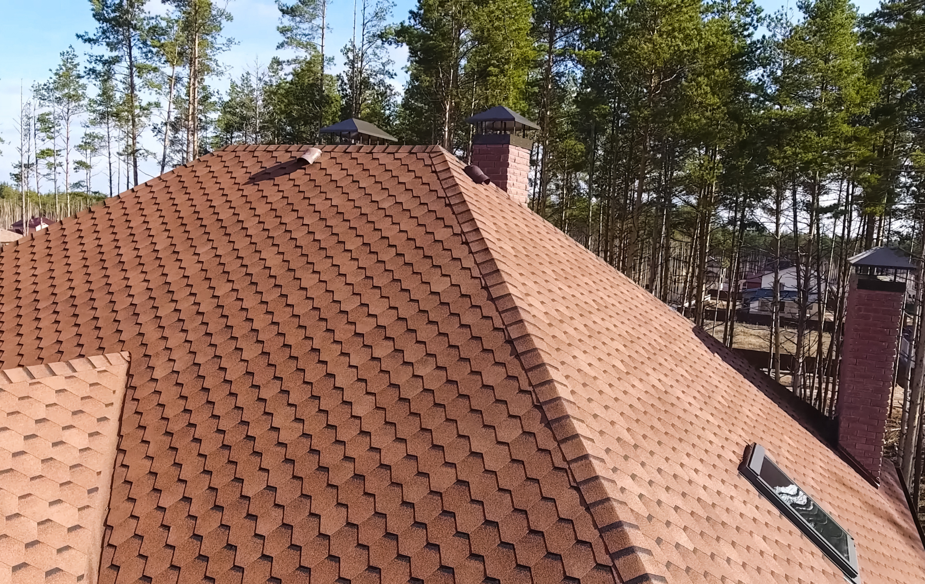 Brown asphalt shingle roof on a house with brick chimneys. Trees in the background.