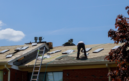 Roofer in safety gear repairs clay tile roof with a hammer.
