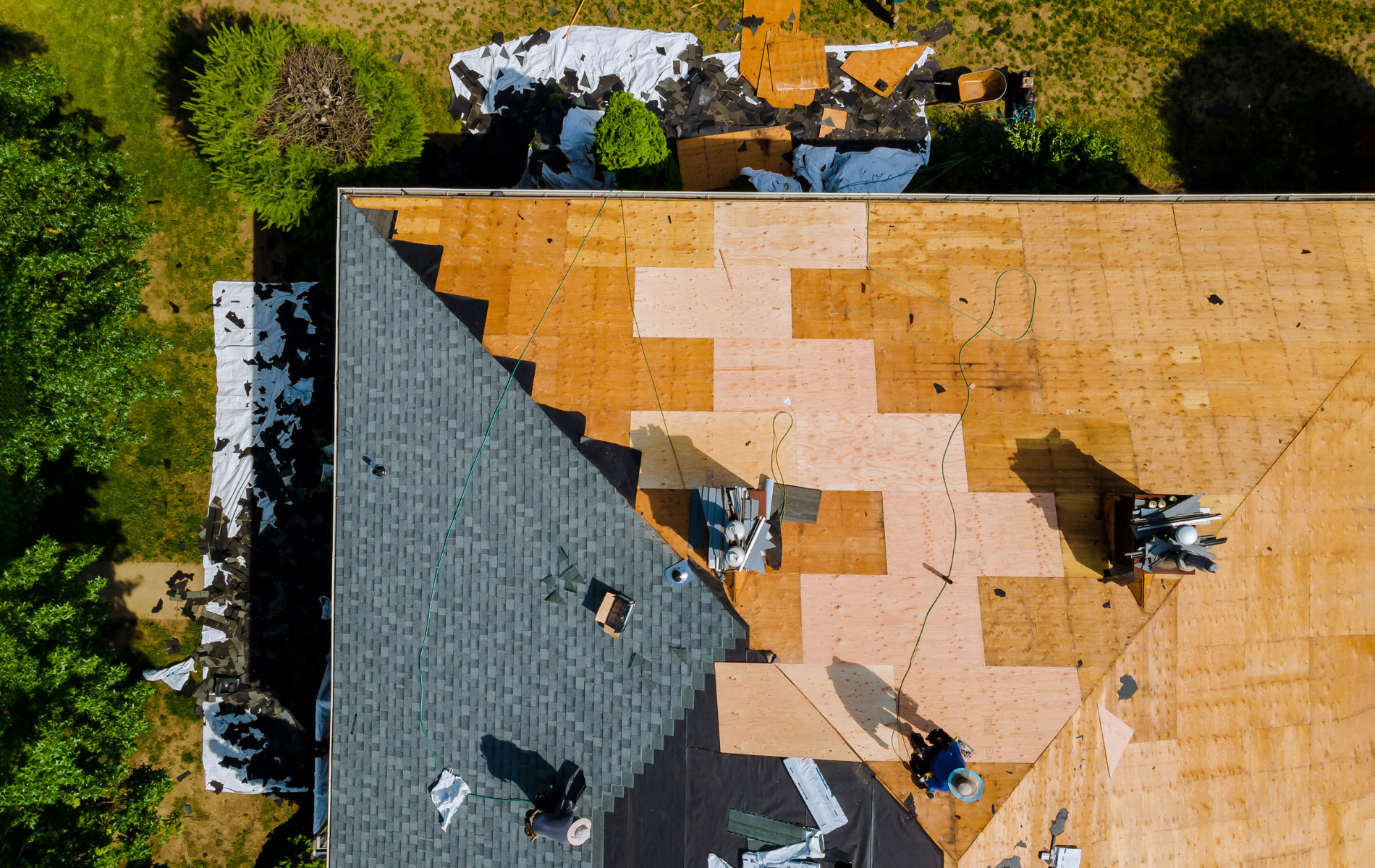 Roof replacement in progress: Workers on a house roof installing new shingles. Sections with old and new roofing.
