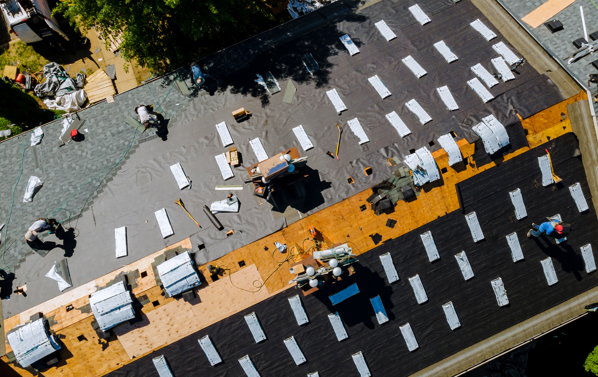 Roofers installing shingles on a commercial building; tools and materials are visible.