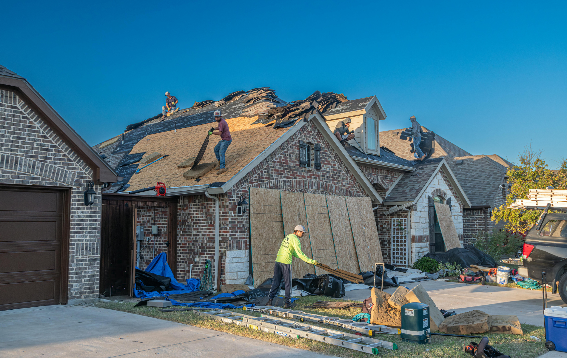 Roofers working on a residential home with damaged shingles, some removed.