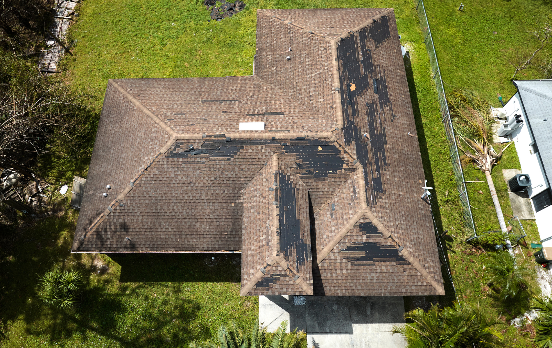 Aerial view of a brown tile roof with several dark patches, surrounded by green grass.