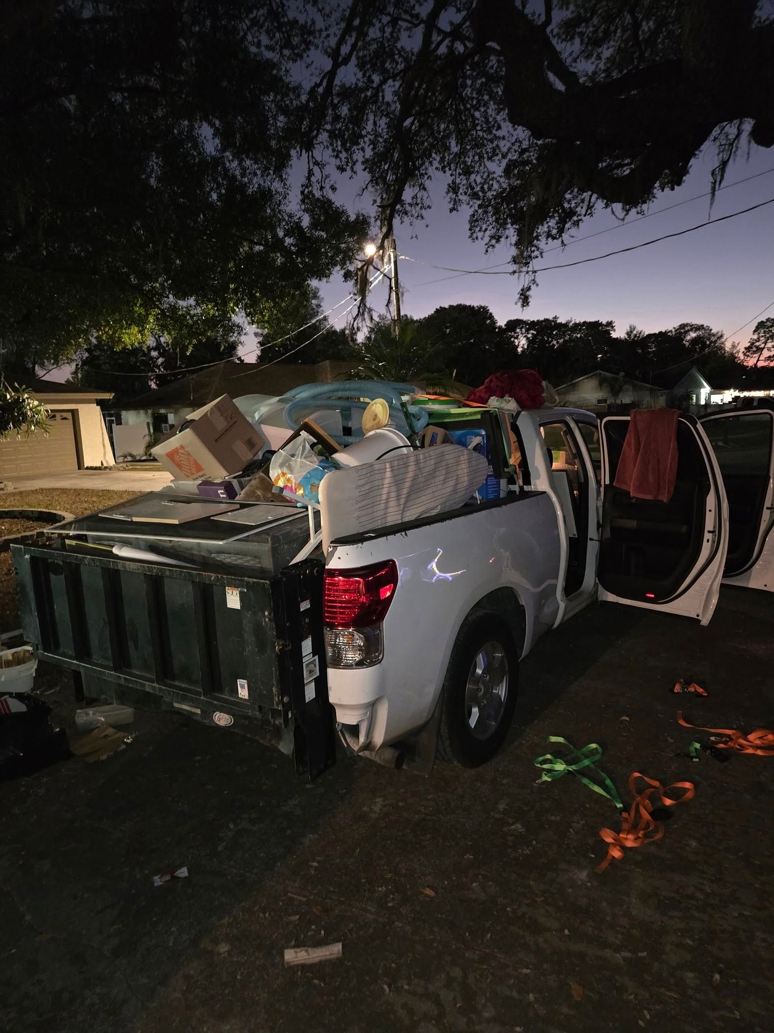 White pickup truck overloaded with household items and furniture at dusk on a dark street.