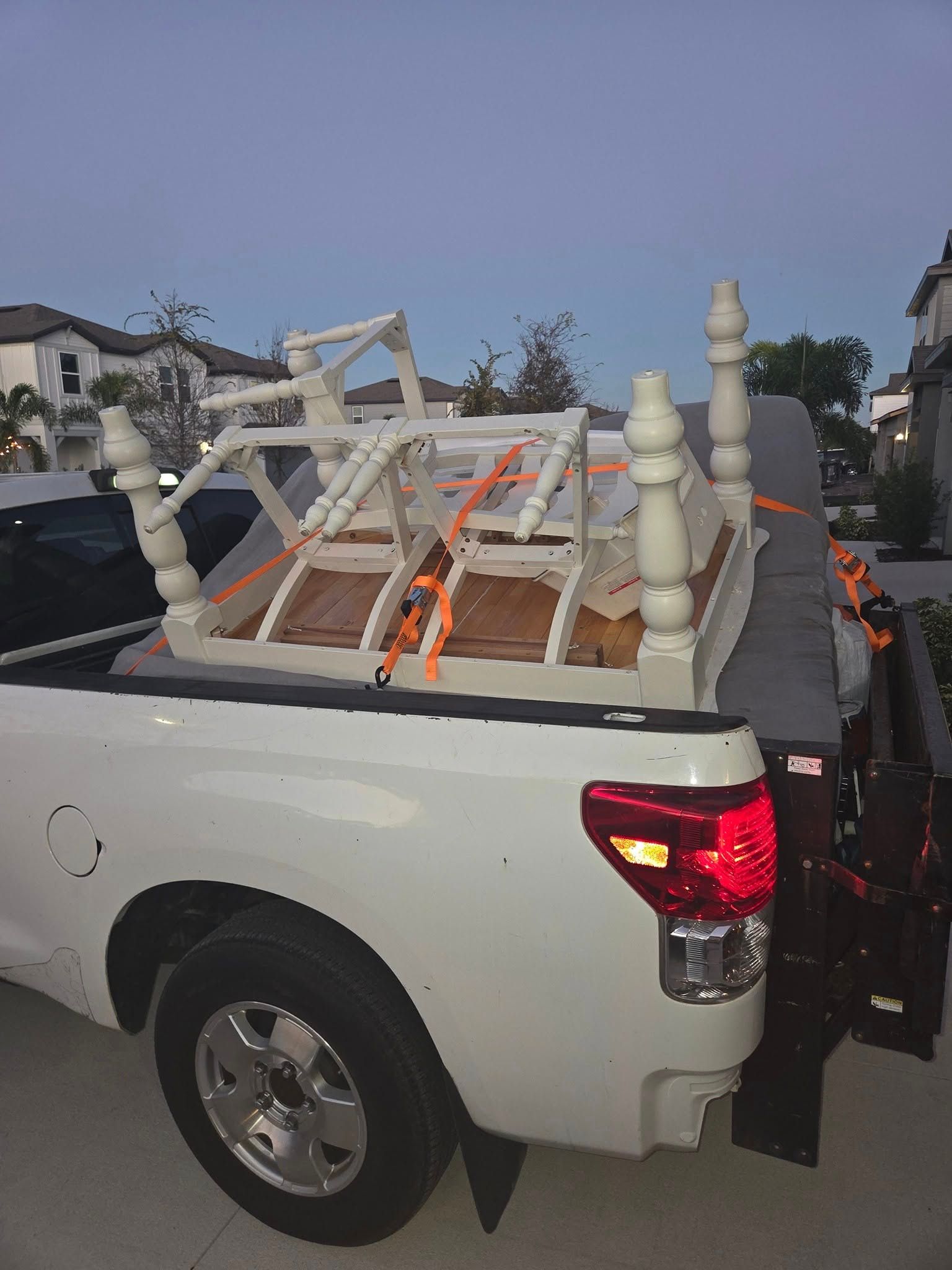 White pickup truck with furniture strapped in the bed, parked outdoors at dusk
