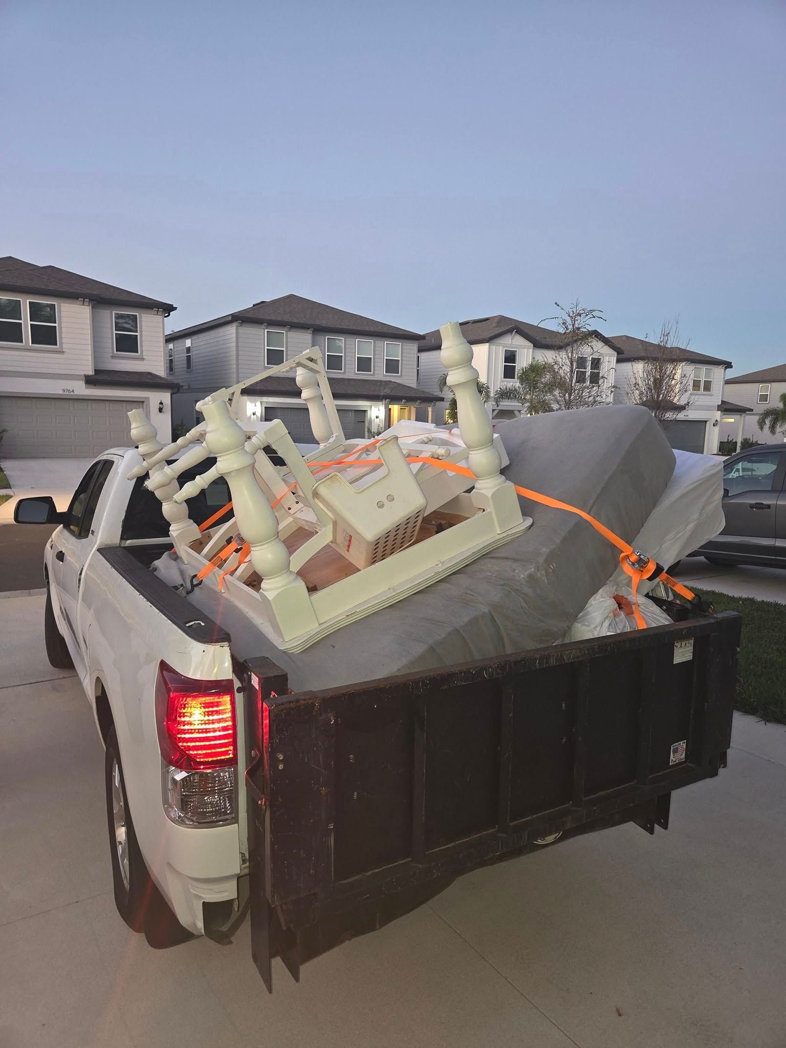 Pickup truck bed loaded with furniture and boxes on a suburban street at dusk