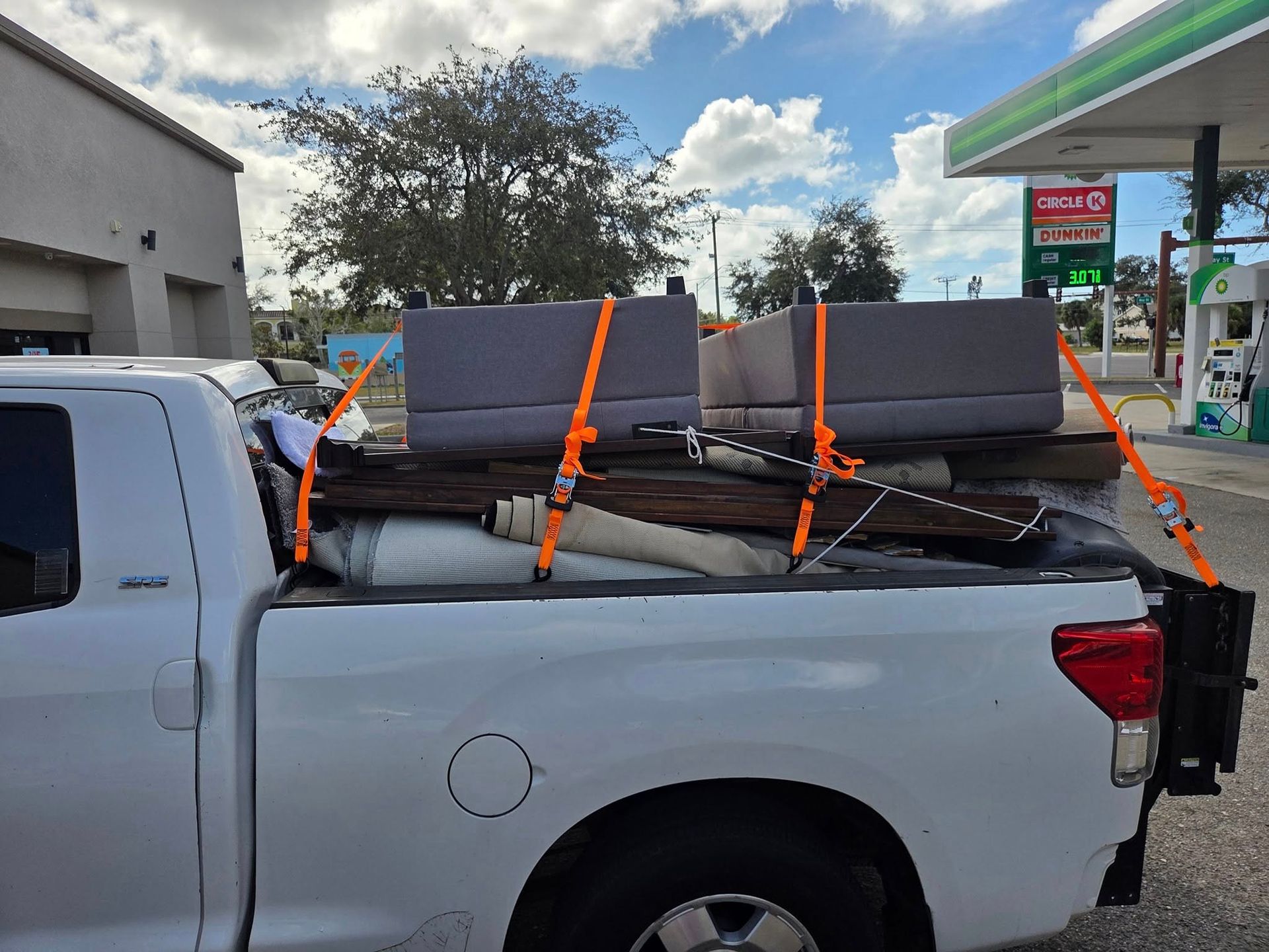 White pickup truck carrying strapped gray blocks at a gas station outdoors