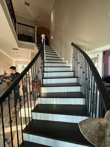 Curved black staircase with white steps in a modern home interior, with people seated in a room at left.